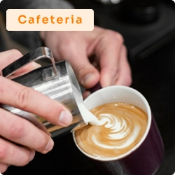 Barista fazendo latte art ao despejar leite vaporizado em xícara de café, representando o ambiente de uma cafeteria.