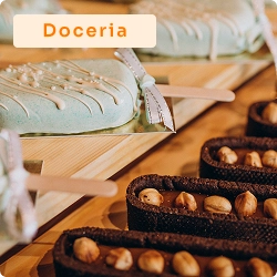 Balcão com doces artesanais, incluindo paletas cobertas e tortinhas com avelãs, em vitrine de doceria decorada.